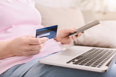 Close-up of woman holding a phone and credit card while balancing laptop on lap