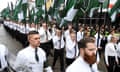 A crowd of mostly men, in shirts, ties and trousers, march on cobblestones holding flags and looking serious