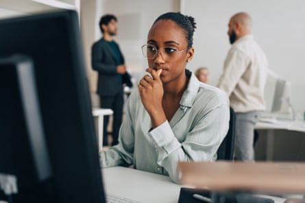 Contemplative young creative professional wearing eyeglasses sitting at desk while working on desktop PC in officeGettyImages-2203405151