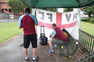 Aston Villa fans watch the teams walk out on a tablet under a gazebo outside the stadium.