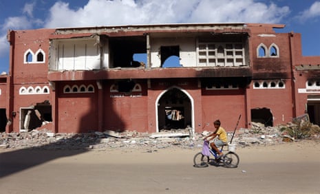 A child rides a bike in front of a destroyed hotel