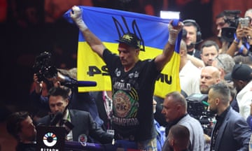 Oleksandr Usyk stands in the ring holding up a flag with Ukraine's national colours of blue and yellow