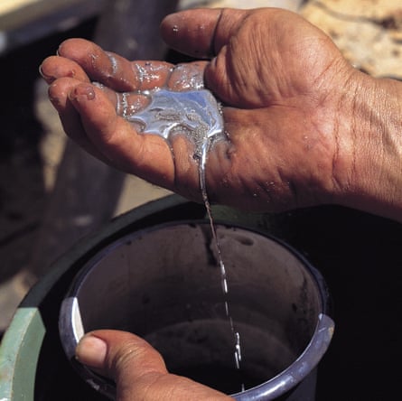 Closeup of a gold prospector’s grubby hand containing a small pool of mercury flowing into a container.