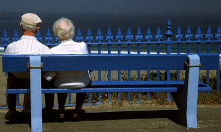 A retired couple sit on bench overlooking the sea.