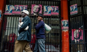 Harare residents walk past campaign posters portraying Zimbabwe’s opposition leader Morgan Tsvangirai on Wednesday.