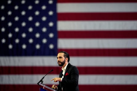 A man talks into a microphone in front of a US flag