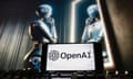 OpenAI logo on a phone screen in front of an image of a robot looking in a mirror