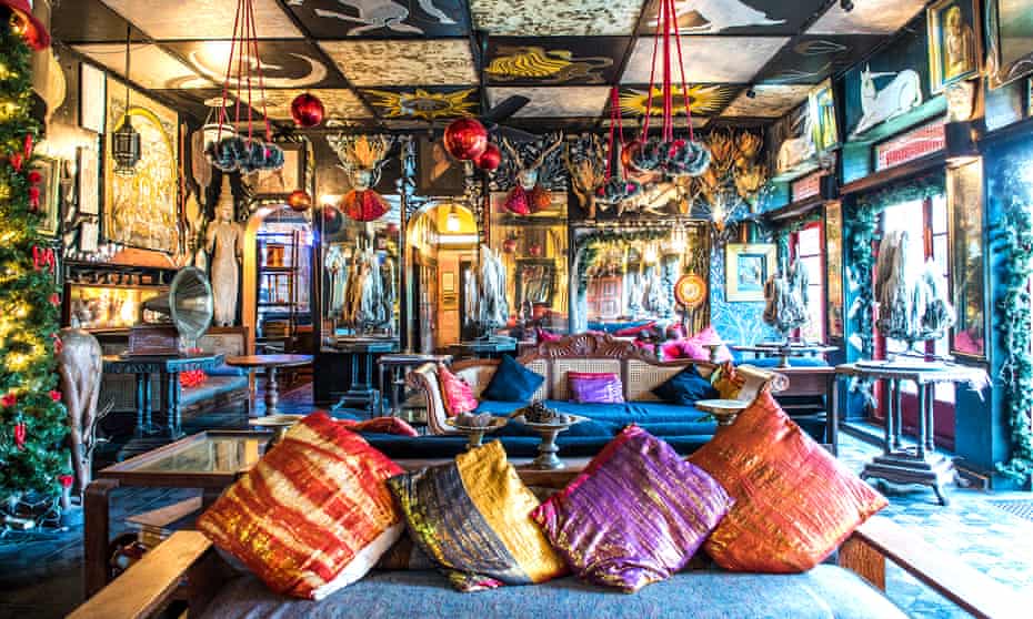 A colourful sitting room with sofas and chandeliers, and murals on the walls at Helga's Folly, a hotel in Kandy, Sri Lanka.
