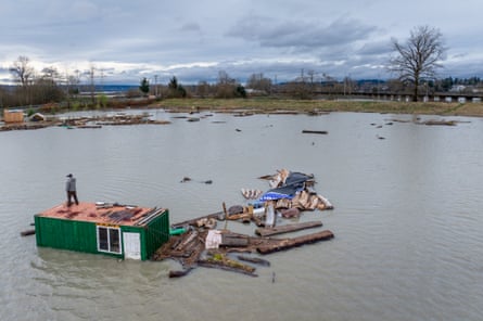 A person standing on the roof of a house surrounded by water.