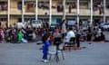 Displaced Palestinians gather in the courtyard of a school, some sitting on chair and others on rugs and blankets