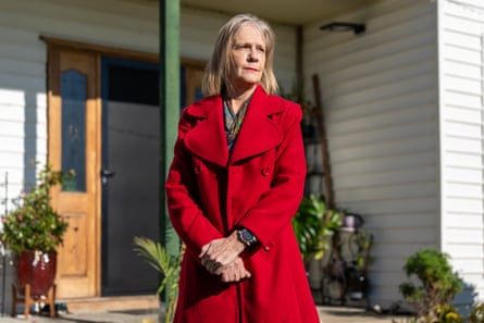 A middle-aged woman wearing a blonde bob and a red coat stares in the distance