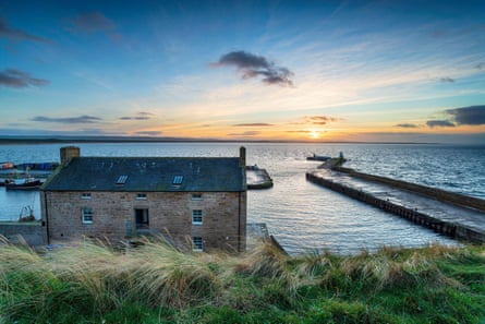 A cottage on the harbour overlooking the sea at sunset.