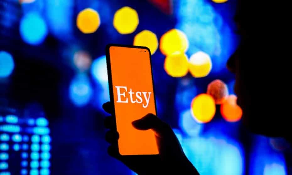 A silhouetted woman holds a smartphone with the Etsy logo displayed on the screen.