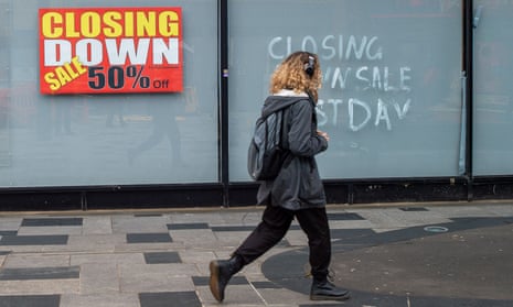 A person wearing headphones and a backpack walks past closing-down sale signs in Slough, Berkshire.