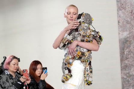 Model holds robot baby as two members of audience take pictures using their smartphones