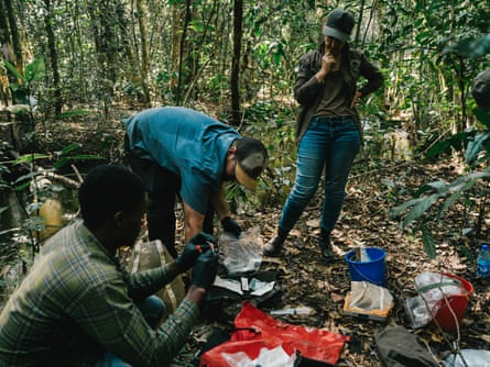 Christine Lain looks down as Dr Chad Keates and Daniel Mukabila go through various pieces of equipment laid out on the forest floor
