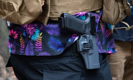 A man wearing a brightly colored Hawaiian shirt carries a firearm clipped to his belt.