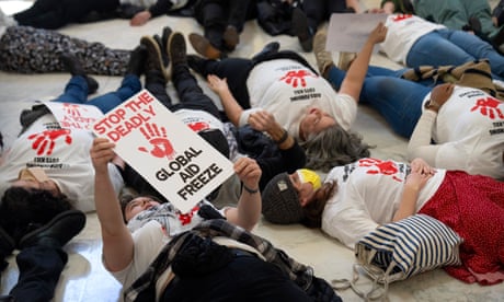 Protesters lie on the floor. One holds a placard saying 'Stop the deadly global aid freeze'