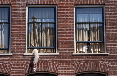 A hose hangs out of the middle window of three in a row on a redbrick building