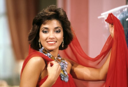 A woman of colour wearing a red chiffon dress with dangly earrings and a big diamond-like necklace