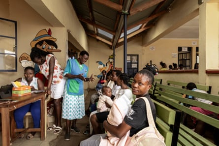 Women and babies sit on wooden benches in a large room