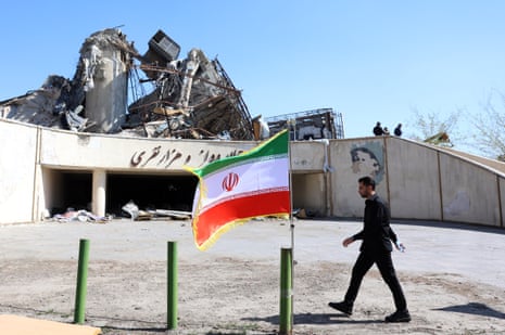 शुक्रवार को ईरान के तेहरान में क्षतिग्रस्त आजादी खेल परिसर के बगल से चलता एक अधिकारी