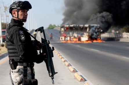 A member of the prosecutor’s office stands guard near a burning bus in Jalisco, Mexico, in February 2026.