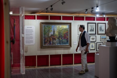 Man stands a looks at large oil painting of the church, adjacent to other smaller pictures