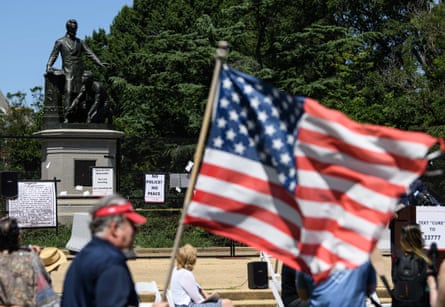 man holds american flag outside by statue of man at protest