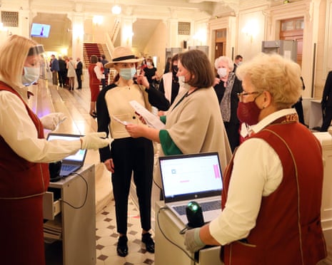Staff in red and white uniforms and masks check tickets in the foyer
