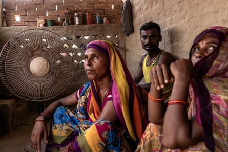 Two women and a man sit by a fan in a room with bare brick walls.