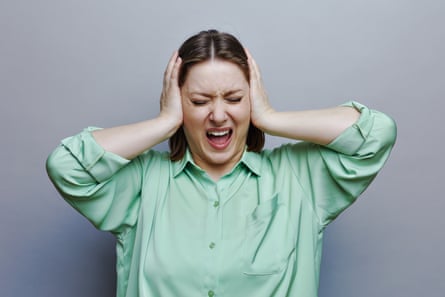 Woman screaming with eyes closed and hands over her ears, on grey studio background, headshot portrait