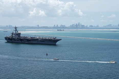 The USS Abraham Lincoln aircraft carrier anchored offshore near Pattaya's skyline, with a small boat passing