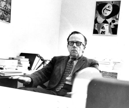 B&W picture of a middle-aged man in a dark suit in his office. There’s a modern artwork on the wall behind him.