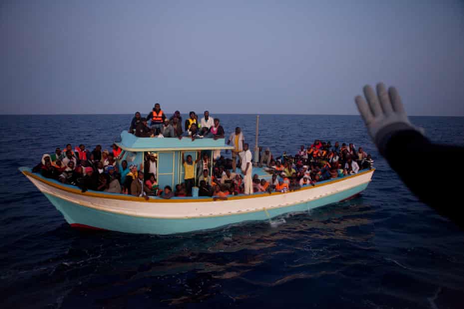 A boat coming from Libya is intercepted by the coastguard, who escort it to the port where police and volunteers are waiting for the 158 people on board.