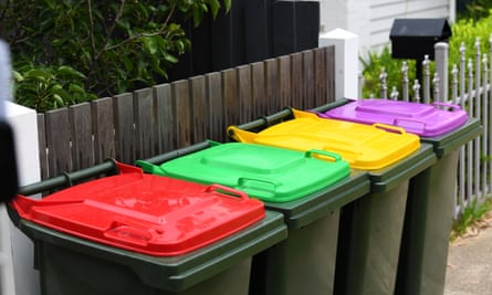 Four wheelie bins lined up outside a house in Victoria with red, green, yellow and purple lids