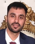 portrait shot showing him in suit and tie; he has short dark hair and a trimmed beard.