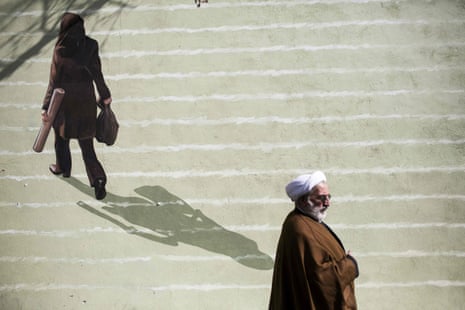 An Iranian clergyman walks past a mural depicting a woman in downtown Tehran.