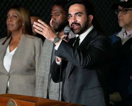 man speaks into a microphone with his hand raised at a news conference