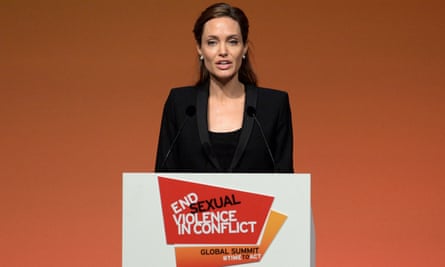 Angelian Jolie wearing a black jacket and top stands behind a lectern which has a sign reading End Sexual Violence in Conflict and Global Summit #TimeToAct