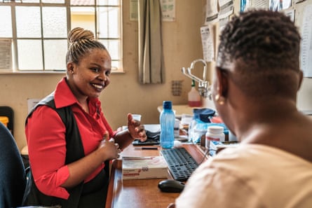 Samukelisiwe Mamba smiles as she sits at a desk with a computer and listens to Precious