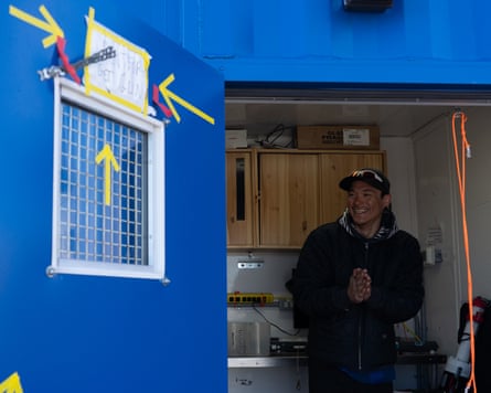 A smiling young Inuit man in a small cabin seen through an open door