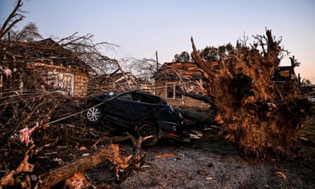 The wreckage of a house and car entangled in tree branches with a rolling fork