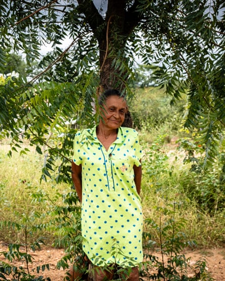 An older woman in a sundress stands under a tree