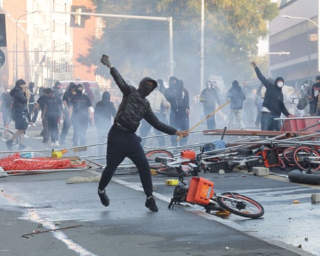 A masked protester mid-jump hurls an object amid smoke during Bologna street clashes