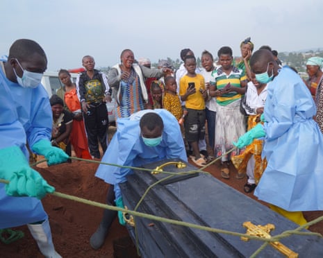 People in protective clothing lower a coffin into a grave