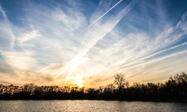 A sunset over a lake and cloud trails from airplanes