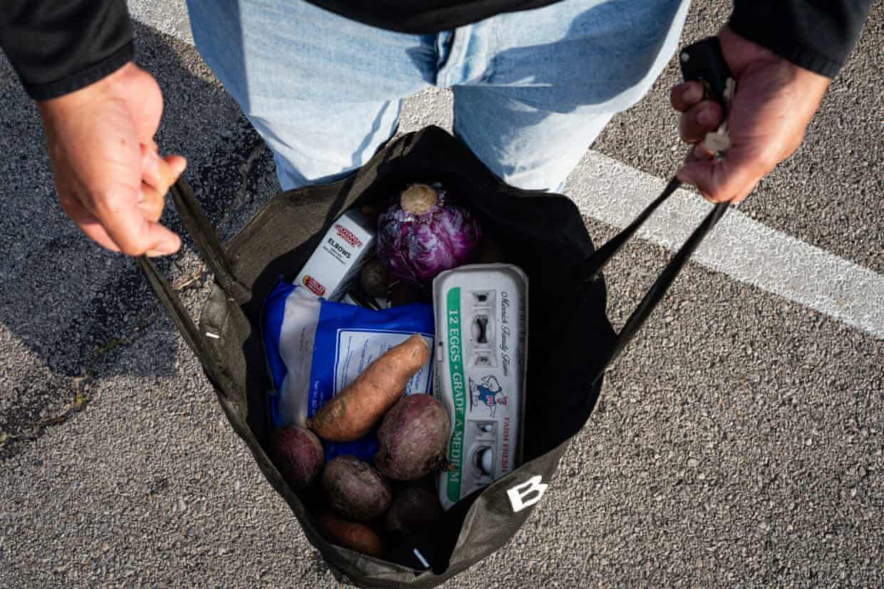 A man holds open a tote bag filled with groceries