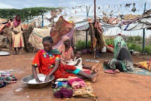 A woman in a red dress sits on the ground washing clothes in an aluminium bowl