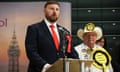 Chris Webb speaking after Labour’s win in the Blackpool South byelection wearing red tie and rosette next to Loony party leader in huge yellow rosette and cowboy hat